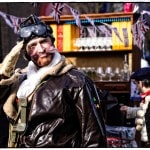 Man in pilot costume saluting at outdoor festival.