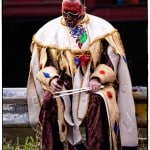 Person in colorful costume sitting with face painted.