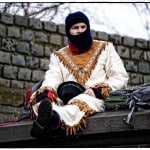 Person in traditional attire sitting on stone ledge.