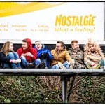 Group sitting under billboard, city background.