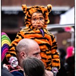 Child in tiger costume on adult's shoulders.