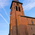 Tall brick church tower under blue sky.