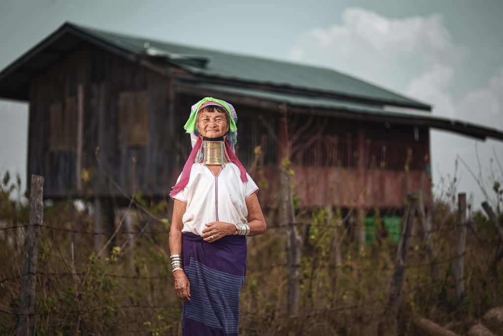 Kayan Lahwi woman in front of a traditional longhouse