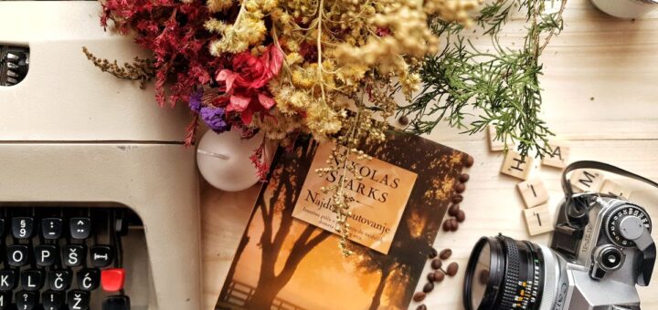 Bunch of flowers and book arranged on wooden table with vintage typewriter and camera