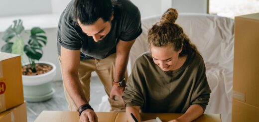 Cheerful diverse couple writing in notebook near boxes before relocation