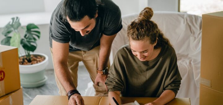 Cheerful diverse couple writing in notebook near boxes before relocation
